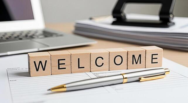 Wooden blocks spelling Welcome resting on a form in a bright office setting conveying a sense of invitation and new beginnings with a laptop and office supplies in the background photo