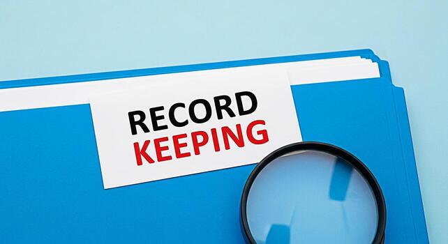 Closeup of a blue file folder with a record keeping label and a magnifying glass on a light blue background representing organization auditing and attention to detail in business management photo