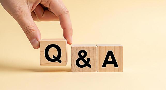 Hand arranging wooden blocks with Q A on a light yellow background representing questions and answers knowledge sharing and interactive communication in a simple and clean studio setting photo