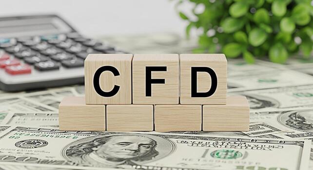 Wooden blocks displaying CFD on a bed of US dollar bills next to a calculator and plant representing Contracts for Difference trading and financial investment strategies for wealth creation photo