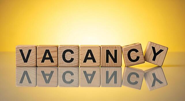 Wooden blocks spelling Vacancy on a reflective surface against a bright yellow background representing job openings and opportunities creating a sense of urgency and anticipation for potential candida photo