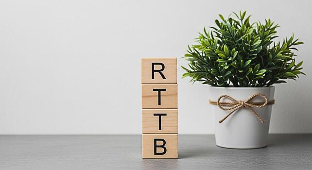 Wooden blocks displaying RTTB next to a potted plant on a gray surface against a white wall symbolizing a structured approach to growth and investment in a clean minimalist environment photo