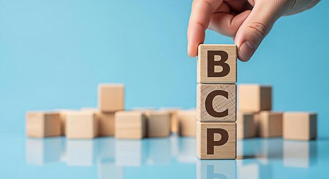 Hand placing a wooden block with the letter B on top of other blocks spelling BCP on a blue background symbolizing Business Continuity Planning and a structured approach to risk management photo