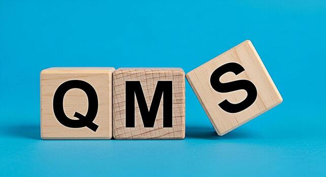 Wooden blocks displaying QMS on a blue surface representing quality management system implementation for continuous improvement and operational excellence in business and manufacturing processes photo