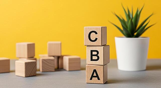 Stack of wooden blocks spelling CBA on a gray surface with a vibrant yellow background and a potted plant representing the concept of basics learning and building blocks of knowledge photo