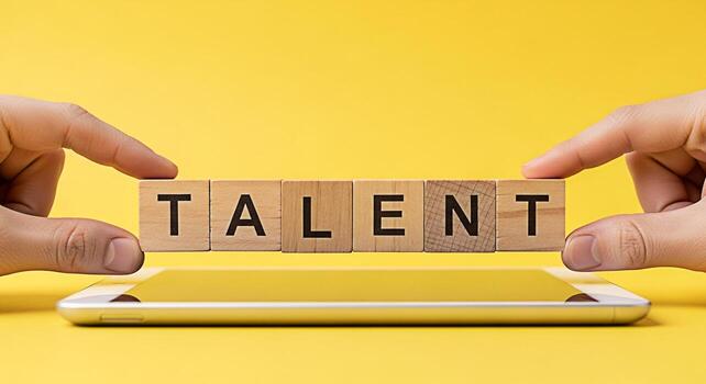 Hands arranging wooden blocks spelling TALENT on a smartphone against a vibrant yellow backdrop symbolizing skill development potential and the importance of nurturing individual abilities in a digita photo