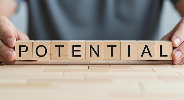 Person arranging wooden blocks spelling POTENTIAL on a wooden surface symbolizing growth and opportunity representing the concept of unlocking hidden abilities and achieving future success with a posi photo