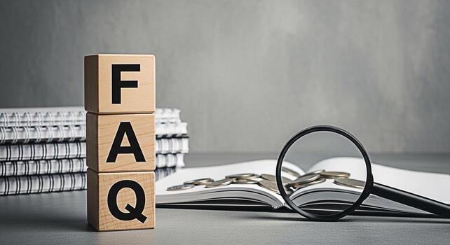 Wooden blocks spelling FAQ are stacked on a desk with notebooks and an open book with coins a magnifying glass nearby representing frequently asked questions and financial literacy in a business setti photo
