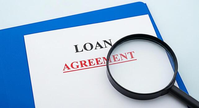 Closeup of a magnifying glass examining a loan agreement document on a blue folder symbolizing financial scrutiny and the importance of understanding contract terms in a professional setting photo