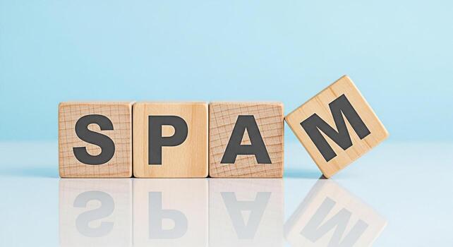 Wooden blocks spelling out SPAM on a reflective surface against a light blue background symbolizing unwanted digital communication and the need for online security and filtering conveying a sense of f photo