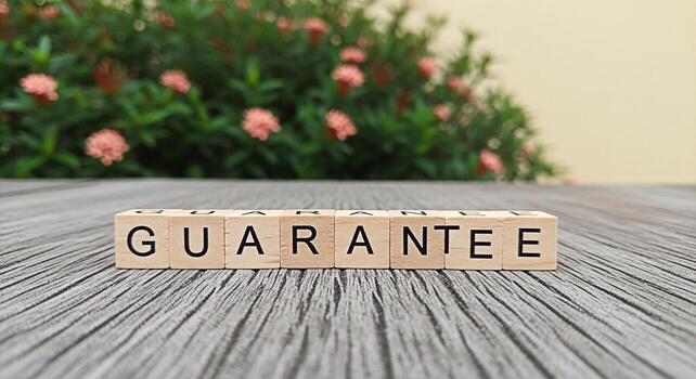 Wooden blocks spelling GUARANTEE on a gray wooden surface with a blurred floral background representing assurance reliability and a promise of quality and customer satisfaction in a natural setting photo