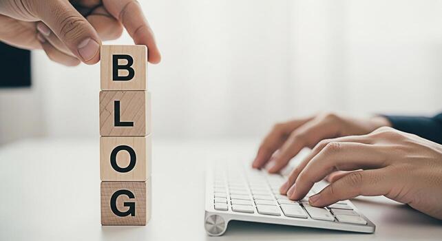 Hands arranging wooden blocks spelling BLOG while typing on a keyboard in a bright modern office symbolizing content creation online presence and the importance of blogging for business success photo