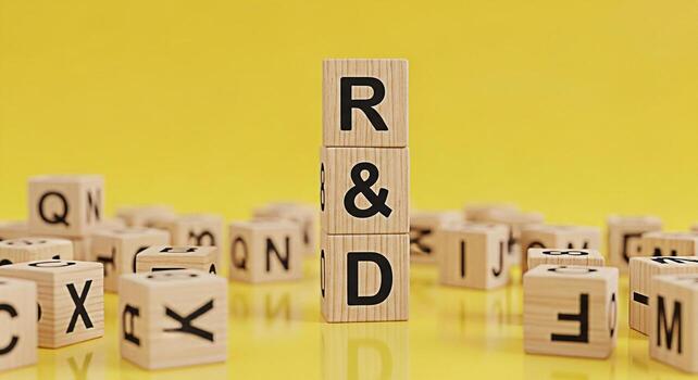 Wooden blocks spelling out RD stacked high on a yellow surface surrounded by scattered letter blocks symbolizing research and development innovation and creative problemsolving in a bright and optimis photo