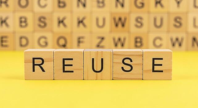 Wooden blocks spelling REUSE on a bright yellow surface promoting environmental awareness and sustainable practices in a studio setting conveying a message of conservation and responsible consumption photo