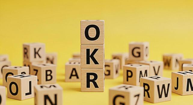 Wooden blocks spelling OKR stacked on a yellow surface surrounded by scattered letter blocks illustrating objectives and key results in a playful and educational setting promoting business strategy an photo