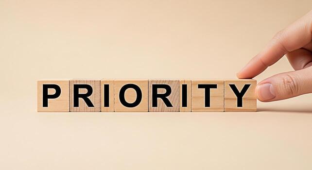 Hand placing wooden blocks spelling PRIORITY on a beige surface emphasizing the importance of prioritization in time management and goal setting for increased productivity and success photo