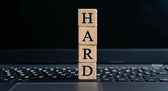 Wooden blocks spelling HARD placed on a laptop keyboard in a dimly lit office symbolizing the concept of challenging work dedication and the effort required to achieve success in the digital age photo