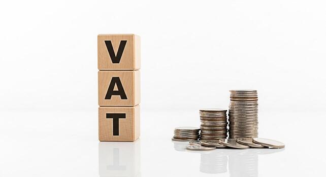 de madera bloques ortografía IVA siguiente a pilas de monedas en un blanco superficie representando valor adicional impuesto y financiero crecimiento en un limpiar minimalista ajuste transporte un sentido de fiscal responsabilidad foto