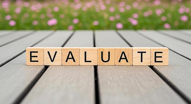 Wooden blocks spelling EVALUATE on a gray wooden surface with a blurred background of pink flowers representing assessment analysis and the importance of critical thinking in a serene setting photo