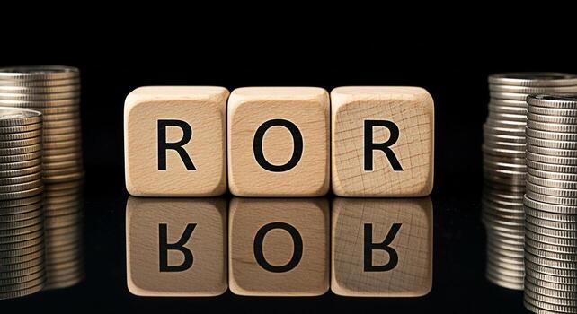 Wooden blocks displaying ROR Rate of Return with stacks of coins on a reflective black surface symbolizing financial investment and success in a business environment conveying a message of growth and photo