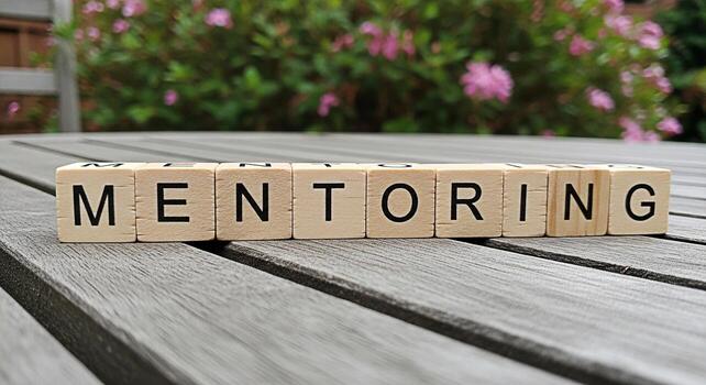 Wooden blocks spelling MENTORING on a weathered wooden table in a garden setting symbolizing guidance support and a positive learning environment for personal and professional development photo