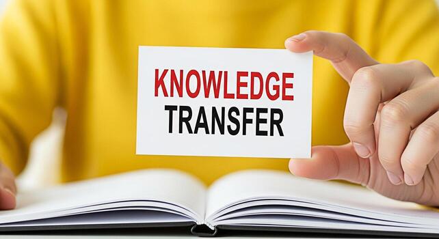 Closeup of a person holding a card with the words Knowledge Transfer in front of an open book symbolizing the sharing of information and skills to foster growth and development in a learning environme photo