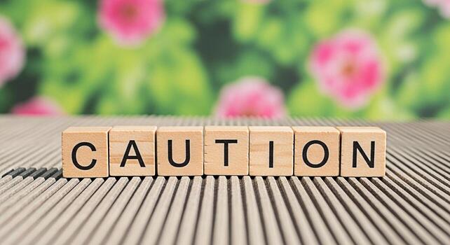 Wooden blocks spelling Caution on a textured surface with a blurred floral background conveying a message of warning and awareness in a natural serene setting emphasizing safety and mindfulness photo
