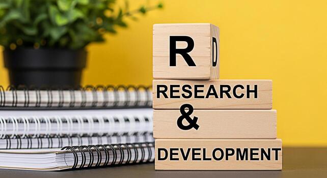 Wooden blocks displaying Research Development stacked on a desk with notebooks and a plant against a yellow background symbolizing innovation progress and strategic planning in a corporate environment photo
