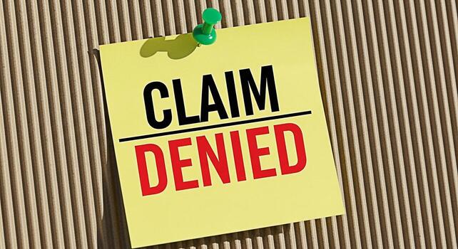Yellow sticky note displaying Claim Denied message pinned on a corrugated cardboard background symbolizing rejection disappointment and the complexities of insurance claims and legal processes photo