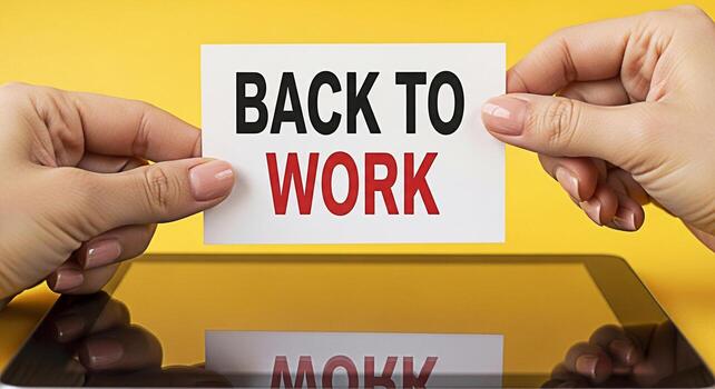 Female hands holding a card with the message Back to Work above a tablet on a yellow background symbolizing a return to the office and a positive attitude towards resuming professional activities photo