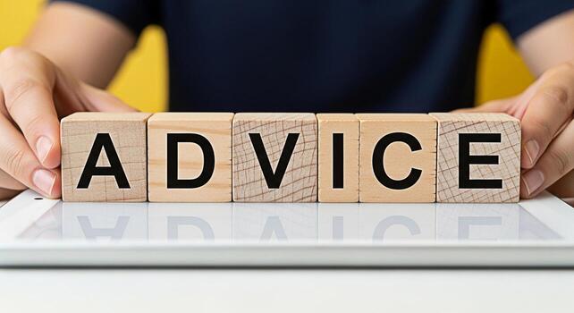 Hands arranging wooden blocks spelling ADVICE on a tablet against a bright yellow background symbolizing guidance mentorship and informed decisionmaking for business and personal growth with a positiv photo