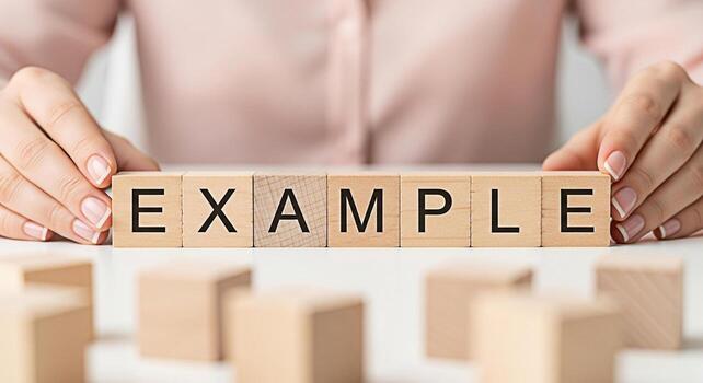 Womans hands arranging wooden blocks spelling EXAMPLE on a white table in a bright clean environment representing clarity demonstration and understanding of concepts and processes photo