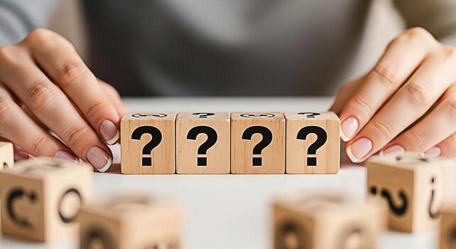 Woman arranging wooden blocks with question marks on a white surface representing uncertainty and the search for answers creating a mood of curiosity and problemsolving in a minimalist setting photo