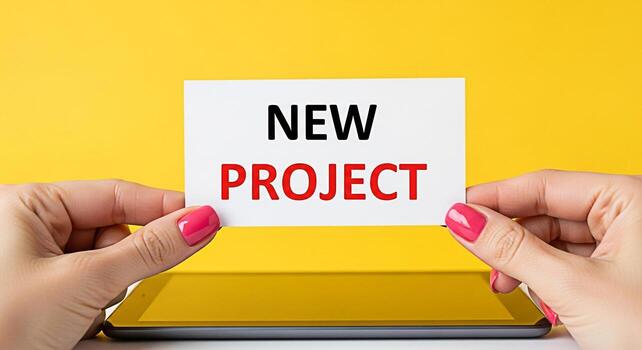 Womans hands holding a card with the words New Project in a bright yellow studio setting symbolizing a fresh start and the excitement of embarking on a new business venture with optimism photo