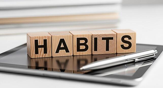 Wooden blocks spelling HABITS resting on a tablet with a pen in a bright modern office setting symbolizing the importance of forming good habits for success and productivity in the workplace photo