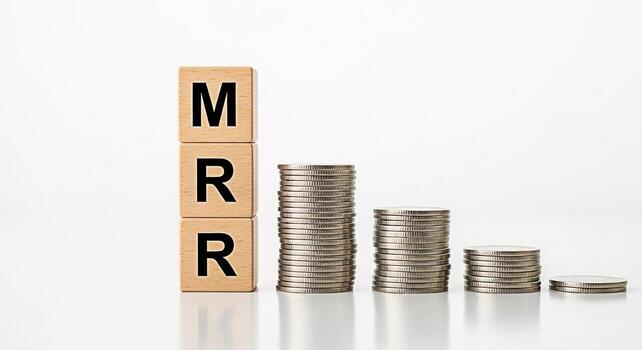 Wooden blocks displaying MRR next to descending stacks of coins on a white surface representing decreasing monthly recurring revenue and financial loss in a minimalist clean setting photo