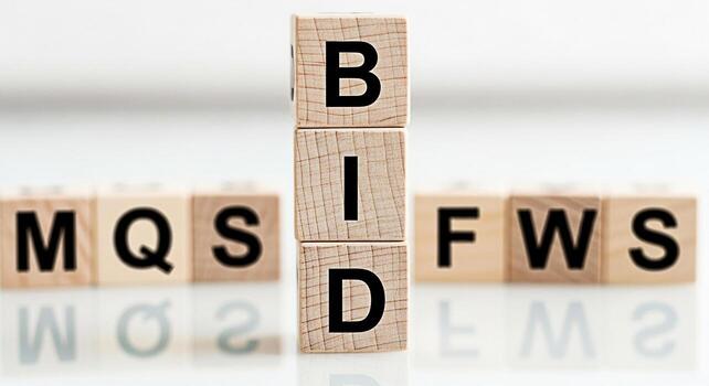 Wooden blocks spelling out BID standing upright on a reflective surface with other blocks showing MQS and FWS in the background conveying a message of business and finance in a minimalist setting photo