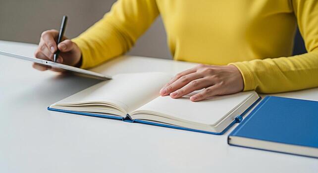 Focused student in a bright room writing notes on a digital tablet and open notebook capturing ideas and planning for success with a modern minimalist workspace and a feeling of productivity photo