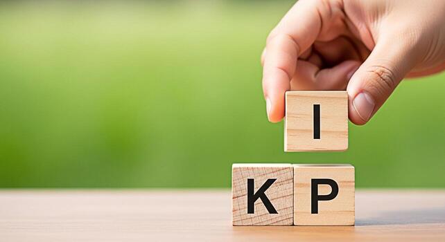 Hand placing a wooden block with the letter I on top of KP blocks on a wooden surface against a blurred green background symbolizing Key Performance Indicators and strategic business objectives photo