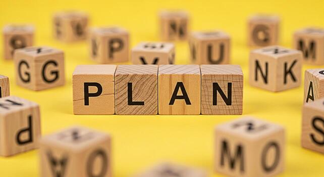 Wooden blocks spelling out PLAN on a bright yellow surface surrounded by other lettered blocks representing strategy and foresight in a playful and educational environment symbolizing organization and photo