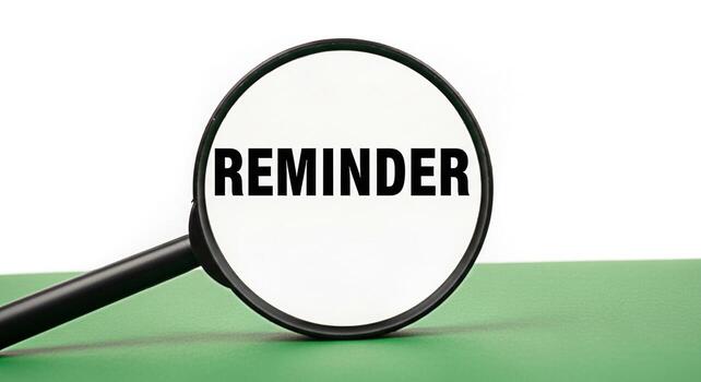 Magnifying glass focusing on the word Reminder on a green surface symbolizing the importance of remembering tasks and deadlines creating a sense of urgency and focus in a clean minimalist setting photo