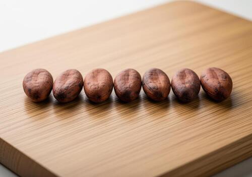 Seven raw cocoa beans aligned in a row on a light brown wooden surface, studio shot photo
