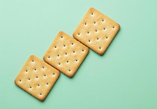 Three golden square crackers arranged diagonally on a smooth pastel mint green background. photo