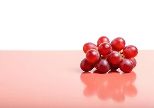 Bright crimson red grape cluster isolated on a reflective salmon pink table photo