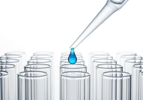 Precision pipette adding a blue drop of chemical liquid into glass test tubes during research. photo