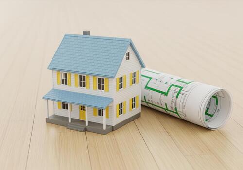 Miniature suburban house model next to rolled architectural blueprints on a wooden surface. photo