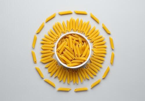 Organized display of golden penne pasta arranged in a circular pattern around a bowl photo