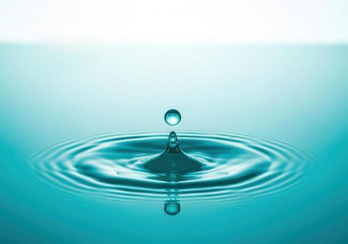 Pristine turquoise water droplet creating perfect splash and concentric ripples. photo