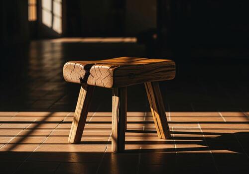 Rustic wooden stool illuminated by dramatic window light and shadows on a tiled floor. photo
