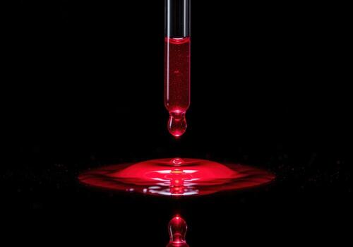 Dramatic close up of a single red drop falling from a glass pipette in a dark lab photo
